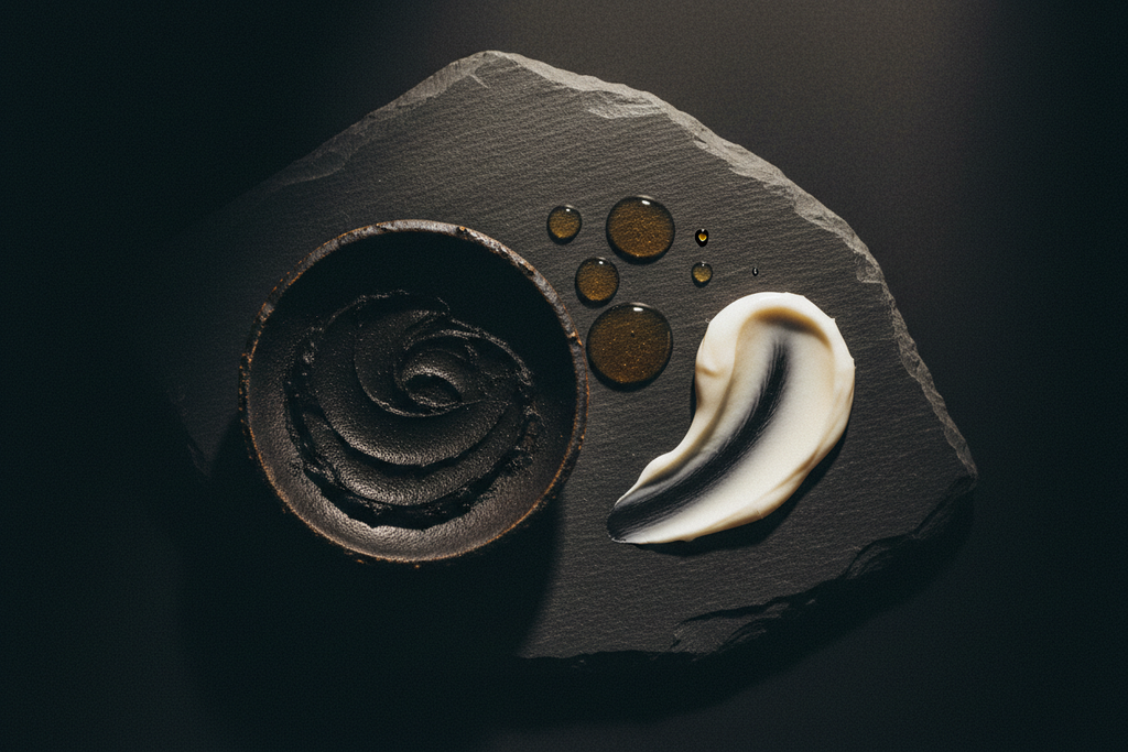 Editorial still life of charcoal mask texture, peptide serum droplets, and night cream on dark stone