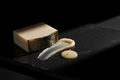 Ivory soap bar, charcoal soap edge, creamy hand balm, and pale candle wax on black lacquered stone